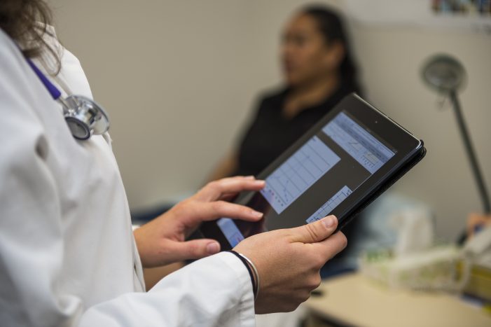 Doctor checking tablet with patient in background